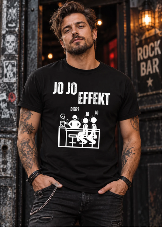 Mann im rockigen Style trägt schwarzes Jo Jo Effekt T-Shirt mit weißem Bierwitz und Strichmännchen-Motiv vor einer Rockbar.