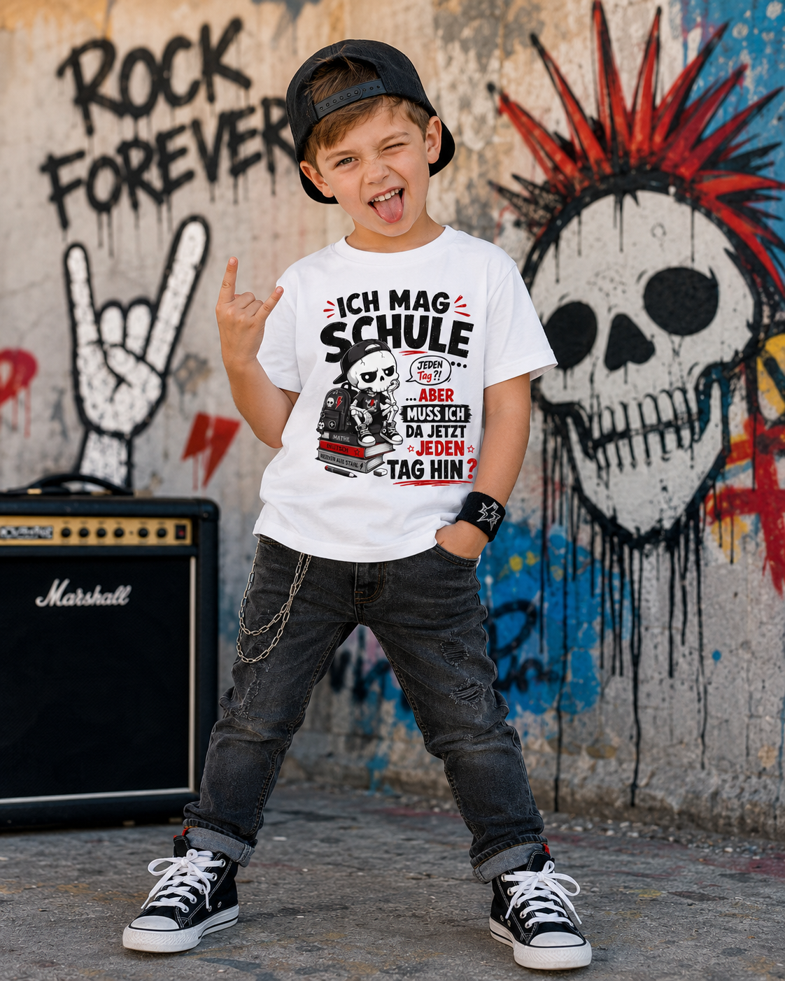 Junge im rockigen Stil trägt ein weißes Kinder T-Shirt mit frechem Skelett-Schulmotiv vor einer Graffitiwand.