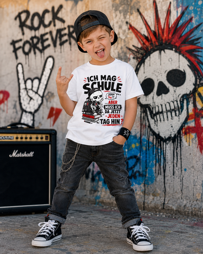 Junge im rockigen Stil trägt ein weißes Kinder T-Shirt mit frechem Skelett-Schulmotiv vor einer Graffitiwand.