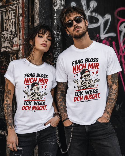 Frau und Mann im rockigen Stil tragen weiße Unisex T-Shirts mit Berliner Skelett-Spruch vor einer dunklen Graffitiwand.