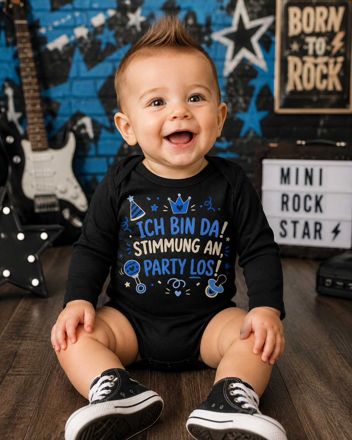 Lachender Baby Junge trägt schwarzen Langarm-Babybody mit dem Spruch Ich bin da Stimmung an Party los vor rockigem blau-schwarzem Hintergrund.