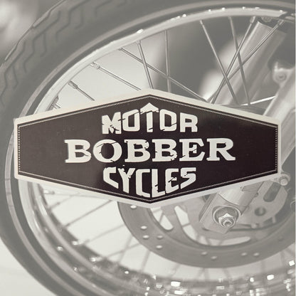 Schwarz-weißer Aufkleber „Motor Bobber Cycles“ vor einem Motorradrad.