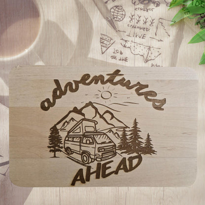Frühstücksbrettchen mit Camper, Bergen und Schriftzug „Adventures Ahead“.
